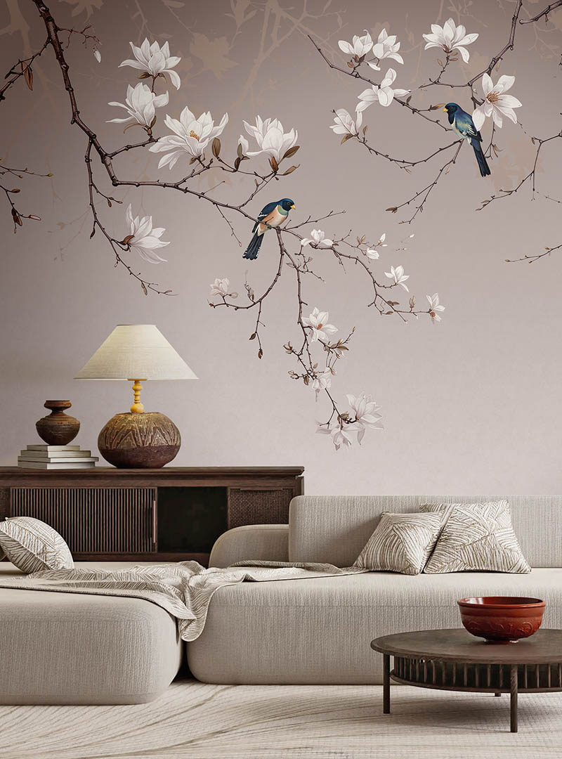 Mudita III botanical bird wallpaper installed above a cream sectional sofa in a warm contemporary living room.